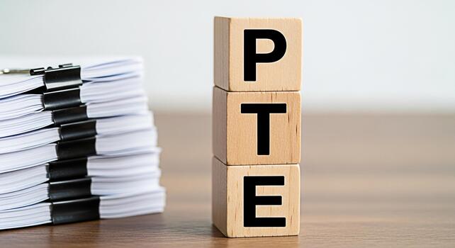 Wooden blocks spelling PTE next to a stack of documents on a wooden desk representing the Pearson Test of English Academic exam preparation and the importance of paperwork and documentation photo