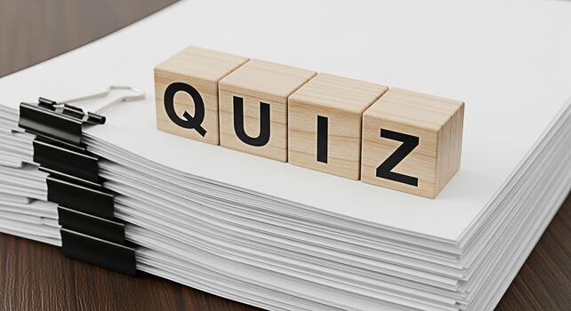 Wooden blocks spelling QUIZ resting on a stack of white paper with binder clips on a dark wood table representing knowledge assessment and learning in a professional and academic setting photo