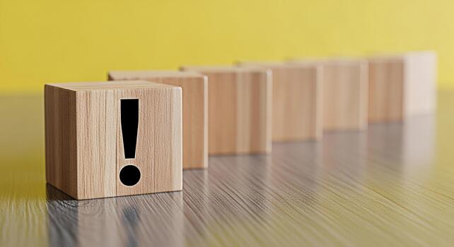 Wooden block displaying an exclamation point symbol standing out among other blocks on a wooden surface against a yellow background representing attention warning and important information photo