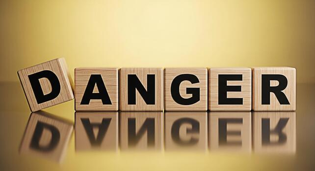 Wooden blocks spelling out DANGER on a reflective surface with one block slightly tilted creating a sense of impending risk and warning against potential hazards in a visually striking composition photo