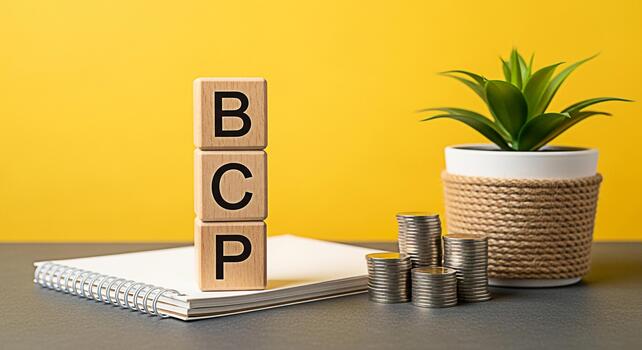 Wooden blocks displaying BCP are stacked on a notebook with coins and a plant against a yellow background representing Business Continuity Planning and financial resilience in a vibrant and organized photo