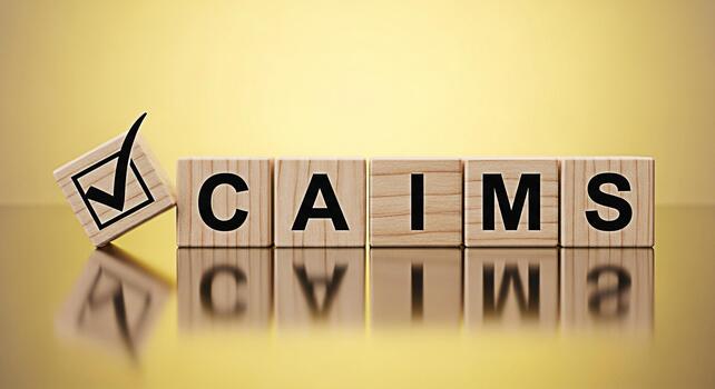 Wooden blocks spelling CLAIMS with a checkmark cube symbolizing validation and approval on a reflective surface against a golden background conveying accuracy and successful completion photo