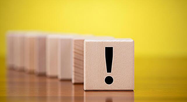 Wooden block displaying an exclamation mark on a wooden surface against a vibrant yellow background symbolizing urgency attention and the importance of clear communication in business and education photo