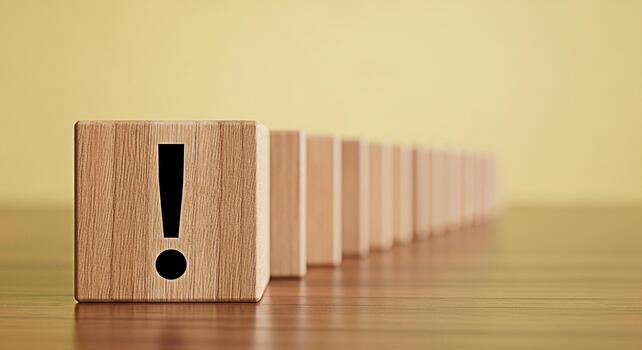 Prominent wooden block with an exclamation point standing out in a line of dominoes on a wooden surface symbolizing risk problem solving and the importance of attention to detail in business and life photo