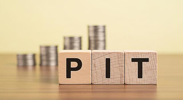 Wooden blocks spelling PIT on a table with stacks of coins in the background symbolizing personal income tax and financial planning creating a sense of fiscal responsibility and awareness photo