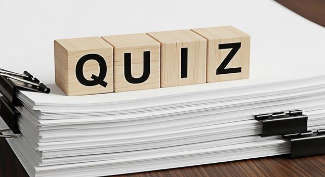 Wooden blocks spelling QUIZ resting on a stack of white paper with binder clips on a wooden desk representing education testing knowledge and the challenge of academic assessments photo