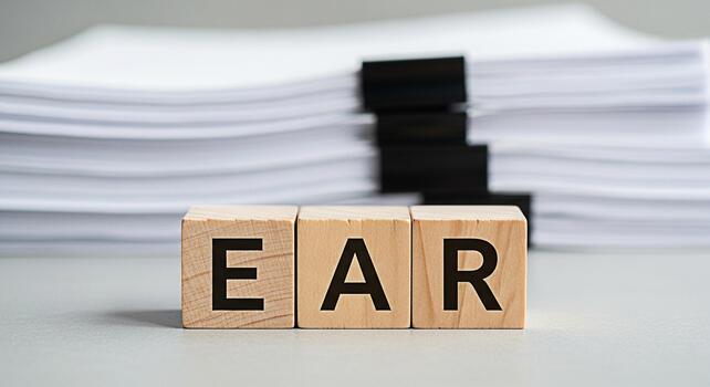 Wooden blocks spelling EAR in a bright office setting representing listening hearing and understanding with a stack of papers in the background conveying focus and attention to detail photo