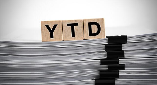 Wooden blocks spelling YTD resting on a large stack of documents in a bright office setting symbolizing yeartodate financial reporting and business performance with a sense of organization and efficie photo