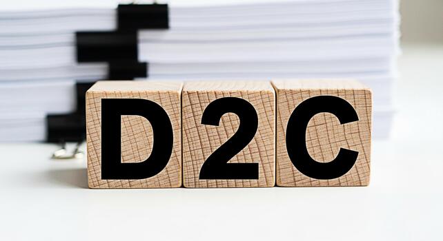Wooden blocks displaying D2C abbreviation on a white desk with a stack of papers representing direct to consumer business model and modern retail strategy in a clean and organized environment photo