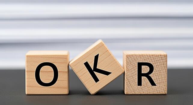 Wooden blocks spelling out OKR on a gray surface in front of a blurred background representing objectives and key results for business strategy and goal setting conveying a sense of clarity and focus photo