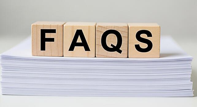 Wooden blocks spelling FAQs resting on a stack of white paper in a bright clean environment representing information access and customer support for easy understanding and quick solutions photo