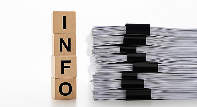 Wooden blocks spelling INFO stand next to a large stack of documents secured with binder clips on a white surface symbolizing information overload paperwork and the need for organization in a business photo