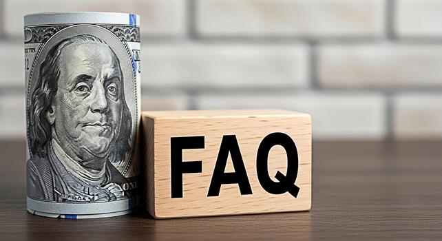 Rolled one hundred dollar bill resting near a wooden block displaying FAQ on a wooden table against a brick wall symbolizing financial questions and answers with a focus on money matters photo