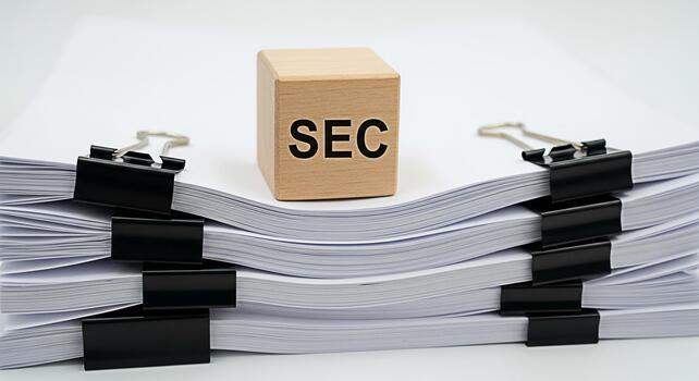 Wooden block with SEC text resting on a stack of white papers secured with black binder clips symbolizing regulatory compliance and financial oversight in a clean professional setting photo