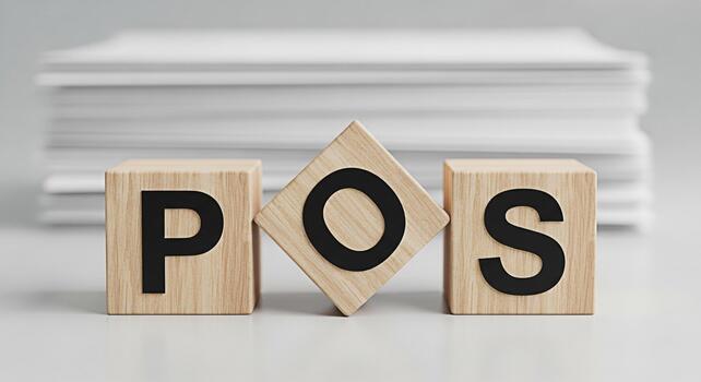 Wooden blocks displaying POS on a white surface with a stack of papers in the background representing point of sale systems and retail technology in a clean and modern setting photo