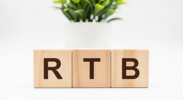 Wooden blocks displaying RTB on a white surface with a green plant in the background symbolizing RealTime Bidding in a clean and minimalist setting conveying a message of modern advertising technology photo