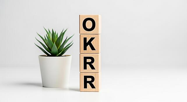 Wooden blocks displaying OKRR acronym standing next to a potted plant on a white table symbolizing objectives and key results for business strategy and goal setting in a clean and modern environment photo