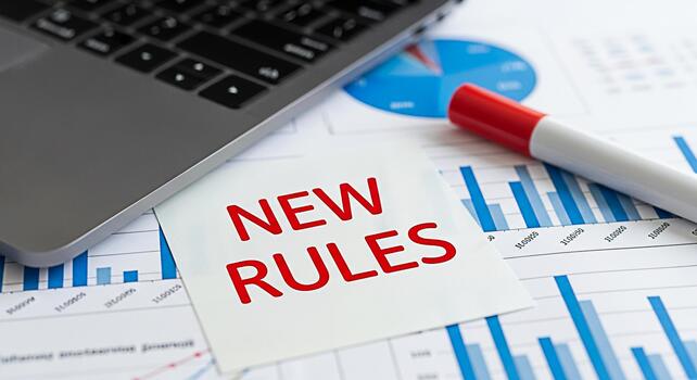 Laptop resting on financial reports with a New Rules note symbolizing regulatory changes and business adaptation in a datadriven environment creating a sense of urgency and strategic planning photo