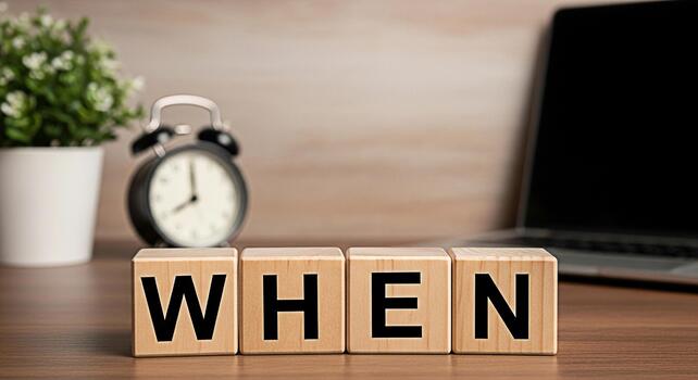 Wooden blocks spelling WHEN on a desk with a laptop and alarm clock symbolizing time management and deadlines in a modern office environment creating a sense of urgency and importance photo