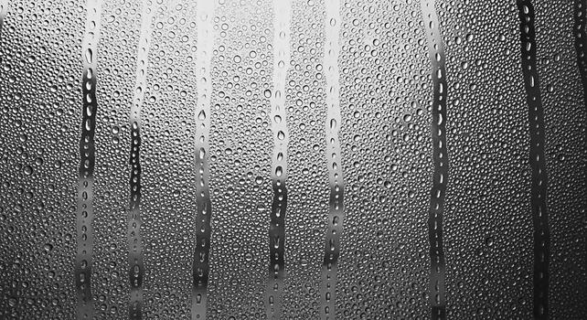 Condensation droplets clinging to a cold glass surface creating a textured pattern with vertical streaks evoking a sense of moisture and coolness in a monochrome abstract background photo