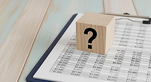 Wooden block with question mark resting on financial report on a wooden desk symbolizing uncertainty in business financial analysis investment decisions and strategic planning in a modern setting photo