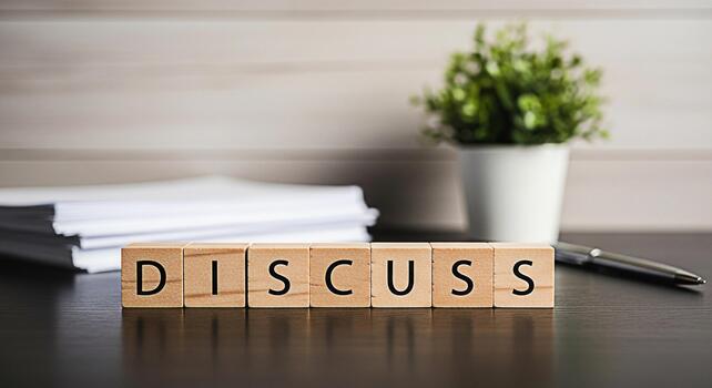 Wooden blocks spelling Discuss on a dark wooden desk in a bright office environment representing collaboration communication and the importance of open dialogue in achieving business goals photo