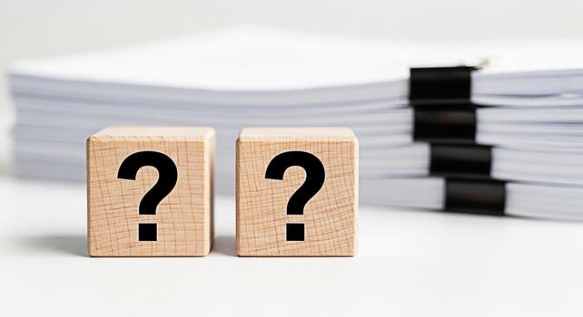 Two wooden blocks displaying question marks sit in front of a stack of papers symbolizing uncertainty and the need for answers in a business or academic setting creating a mood of inquiry and problems photo