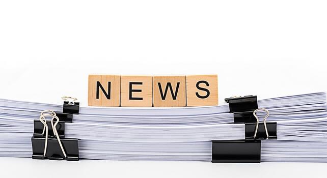 Wooden blocks spelling NEWS sitting atop a stack of papers secured with binder clips on a white background representing information overload and the constant flow of current events in a fastpaced worl photo