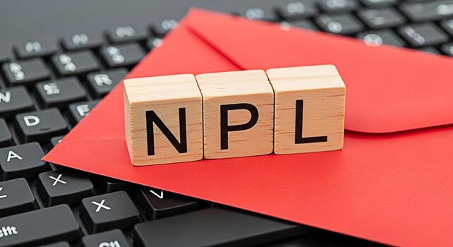 Wooden blocks spelling NPL resting on a red envelope atop a black computer keyboard symbolizing nonperforming loans and financial challenges in a modern business environment conveying a serious mood photo