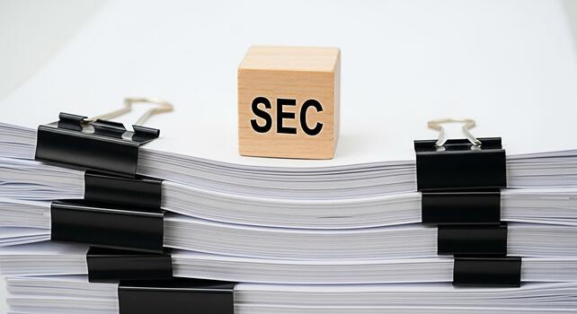 Wooden block displaying SEC sitting atop a stack of documents secured with binder clips in a bright minimalist office setting symbolizing regulatory compliance and financial oversight with a sense of photo