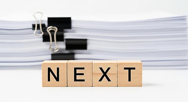 Wooden blocks spelling NEXT stand prominently in a bright office setting symbolizing future projects and opportunities amidst a backdrop of organized documents and paperwork conveying a sense of antic photo