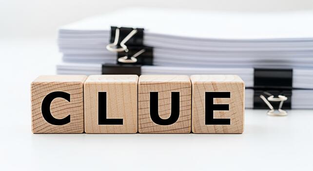 Wooden blocks spelling CLUE resting on a white surface with a stack of documents in the background suggesting investigation mystery or problemsolving in a professional or academic setting photo