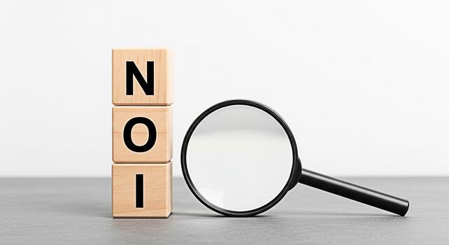Wooden blocks displaying NOI being examined with a magnifying glass on a gray surface representing Net Operating Income analysis and financial due diligence in a clean minimalist setting photo