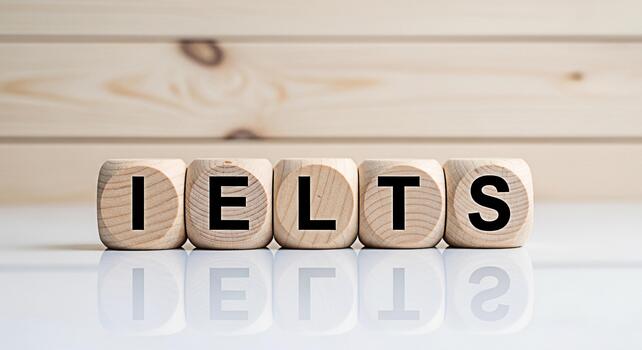 Wooden blocks spelling IELTS on a reflective surface against a light wood background representing the International English Language Testing System and the concept of language proficiency testing photo