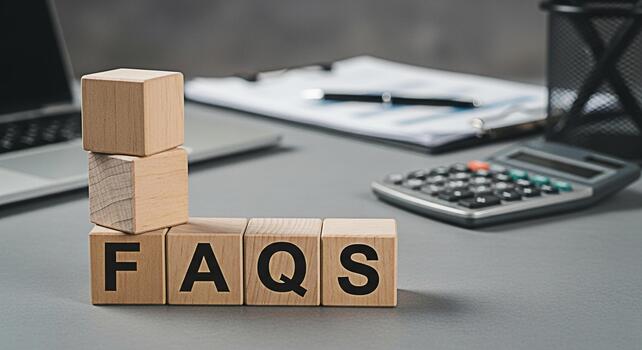 Wooden blocks spelling FAQs on a gray desk with a laptop calculator and documents representing information and support for customers and clients in a professional setting photo