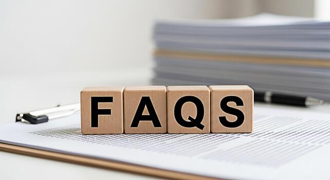 Wooden blocks spelling FAQs resting on a document with a pen and stack of papers in the background representing information support and frequently asked questions in a business setting photo