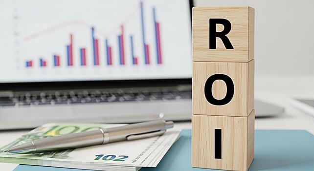 Wooden blocks displaying ROI on a desk with a laptop showing a financial graph symbolizing investment analysis and the potential for high returns in a modern business environment fostering a sense of photo