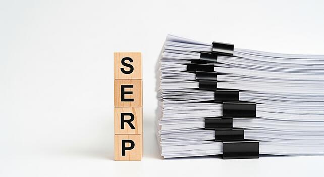 Wooden blocks spelling SERP stand next to a large stack of documents secured with binder clips on a white surface representing search engine optimization and the importance of content creation photo