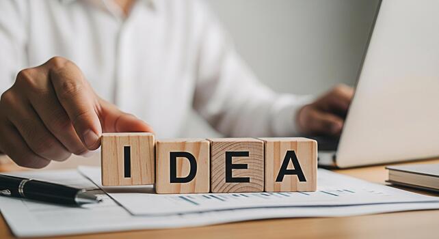 Businessman arranging wooden blocks spelling IDEA on a desk with a laptop in a bright office symbolizing creativity innovation and problemsolving in a modern business environment photo