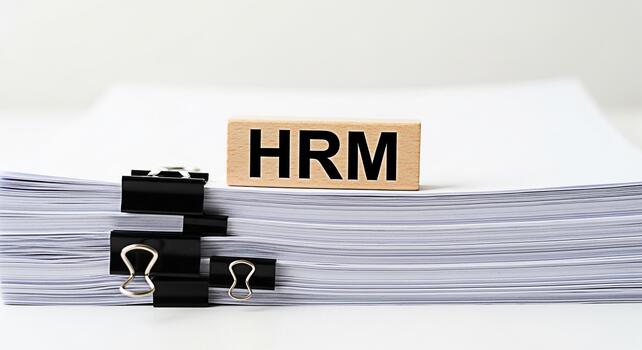 HRM block resting on a stack of documents secured with binder clips in a bright office setting representing human resources management and the importance of organized paperwork conveying efficiency an photo