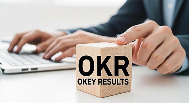 Business professional typing on a laptop in a bright office setting focusing on OKR Objectives and Key Results displayed on a wooden block symbolizing goal setting and achievement photo