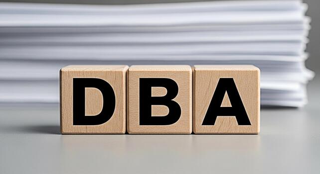 Wooden blocks spelling DBA on a gray surface with a stack of papers in the background representing business operations and legal compliance in a professional and organized environment conveying a sens photo