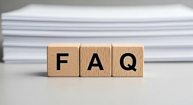 Wooden blocks spelling FAQ on a gray surface with a stack of papers in the background representing frequently asked questions and information resources in a clean and minimalist setting photo