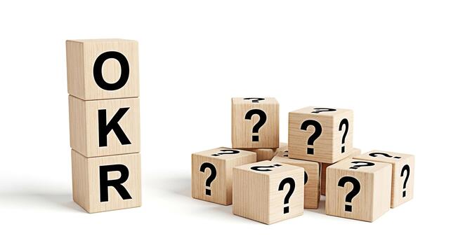 Wooden blocks displaying OKR standing tall next to a group of question mark blocks on a white surface representing business objectives and key results with an element of uncertainty and inquiry photo