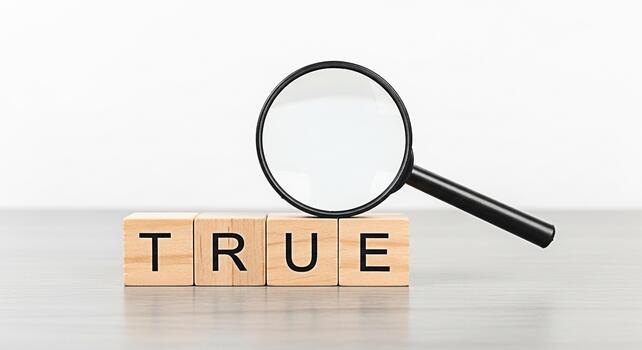 Magnifying glass examining wooden blocks spelling TRUE on a neutral surface symbolizing verification accuracy and the importance of truth in a clear and straightforward manner photo