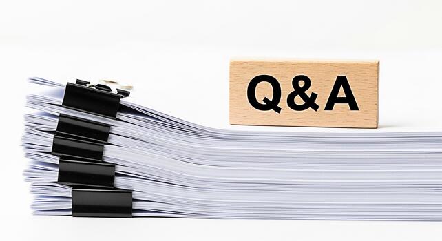 Stack of documents with black binder clips next to a wooden block with QA text on a white background representing questions and answers knowledge and information in a business setting photo
