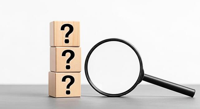 Stack of wooden blocks displaying question marks being examined with a magnifying glass on a gray surface symbolizing inquiry uncertainty and the search for answers in a minimalist setting photo