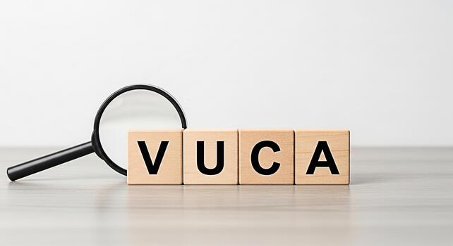 Wooden blocks spelling VUCA being examined with a magnifying glass on a table against a white background representing volatility uncertainty complexity and ambiguity in business and strategic planning photo