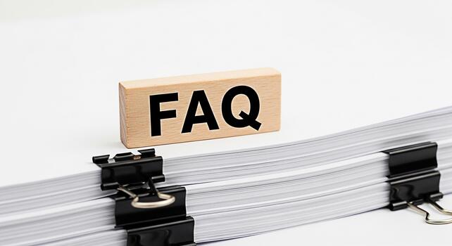 Wooden block displaying FAQ resting on a stack of papers secured with binder clips symbolizing readily available answers and information in a clean organized setting promoting clarity and efficiency photo