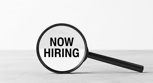 Magnifying glass focusing on Now Hiring text on a neutral surface symbolizing recruitment and job opportunities creating a sense of urgency and highlighting the availability of new positions photo